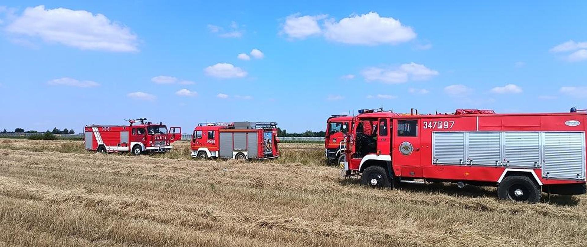 Samochody strażackie stoją na ściernisku.