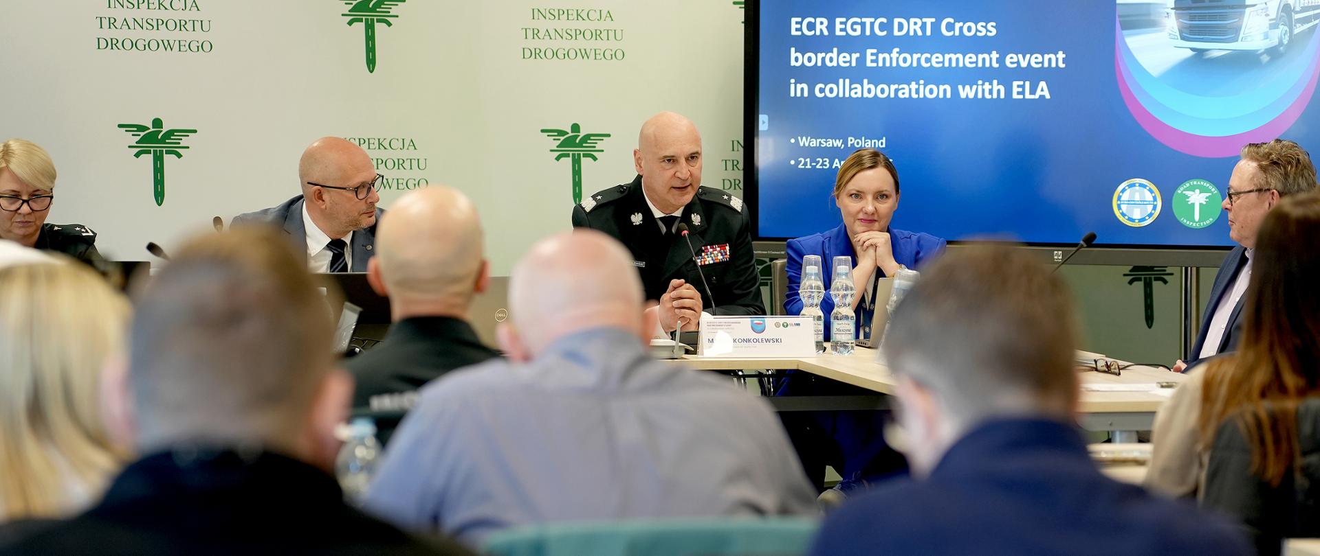 Panel dyskusyjny z udziałem przedstawicieli instytucji transportowych siedzących przy stole konferencyjnym, przemawiających do uczestników wydarzenia w sali szkoleniowej.