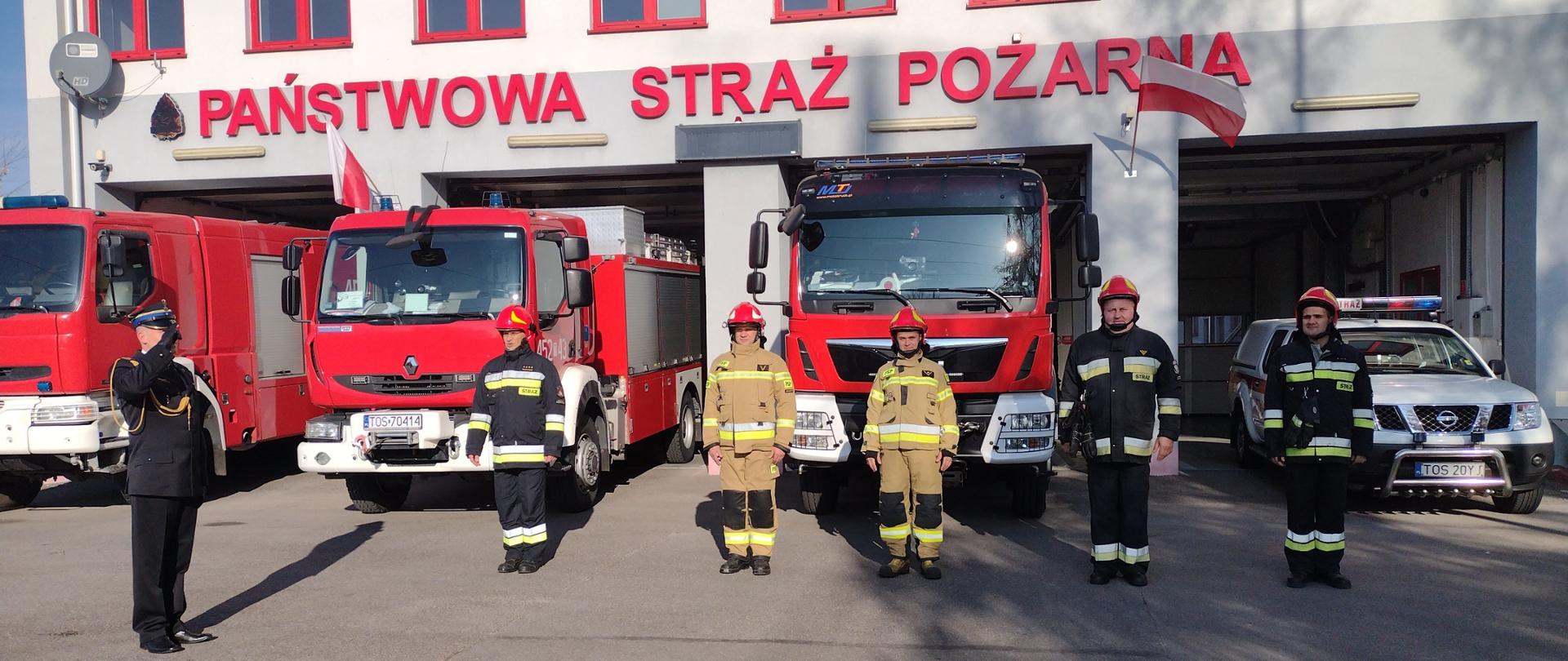 Strażacy na tle wystawionych prze garaż samochodów pożarniczych