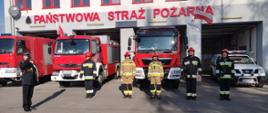 Strażacy na tle wystawionych prze garaż samochodów pożarniczych
