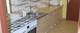 Miejsca noclegowe w siedzibie OSP. Pomieszczenie kuchenne, w którym znajdują się dwie kuchenki gazowe, zlewozmywak oraz meble. Na blacie stoją trzy czajniki bezprzewodowe oraz kuchenka mikrofalowa.