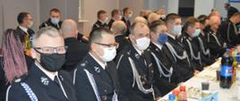Zjazd OP ZOSP RP w Rawiczu. Sala wiejska w Rogożewie. Po obu stronach stołów zasiadają uczestnicy Zjazdu. Wszyscy w mundurach wyjściowych. Na twarzach mają maseczki ochronne. Na stole ustawione są kubki i napoje. W tle stół prezydialny i baner.