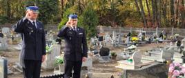 dwóch strażaków w mundurach oddaje hołd przy grobie zmarłego strażaka