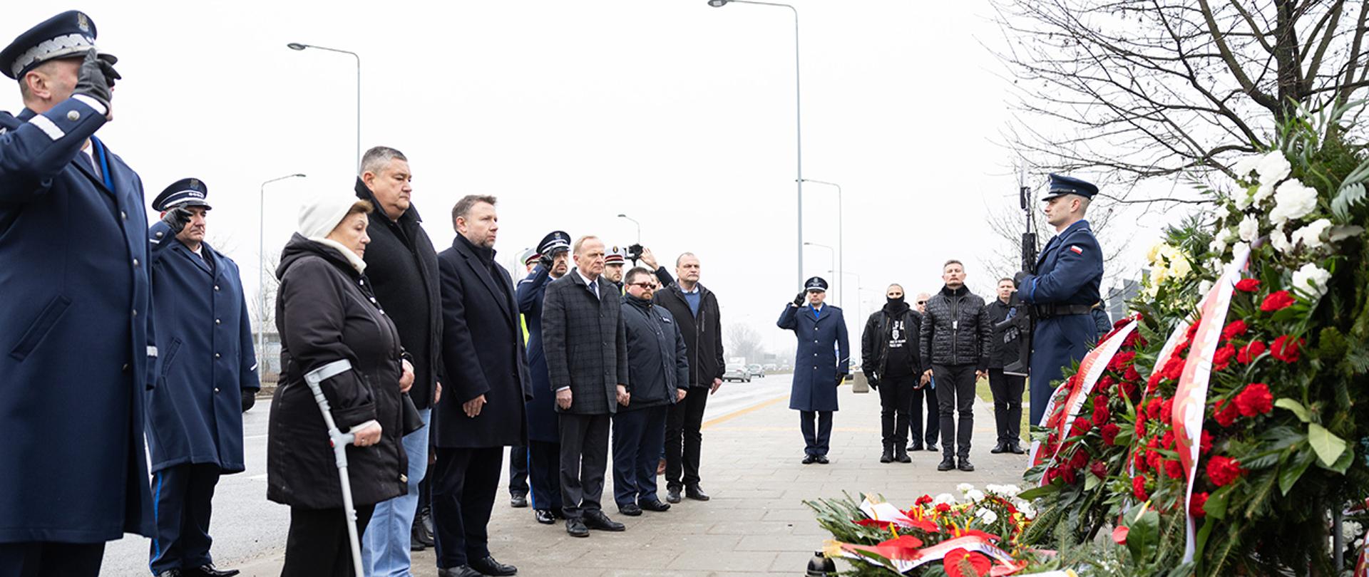 Zdjęcie przedstawia ministra Marcina Kierwińskiego, wiceministra Czesława Mroczka, Komendanta Głównego Policji Michała Boronia i rodzinę zmarłego Andrzeja Struja po złożeniu kwiatów pod pomnik upamiętniający tragedię.