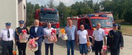 Druhowie ochotniczej straży pożarnej zaproszeni goście oraz funkcjonariusze Państwowej Straży Pożarnej stoją obok siebie za nimi ustawione są trzy samochody gaśnicze.