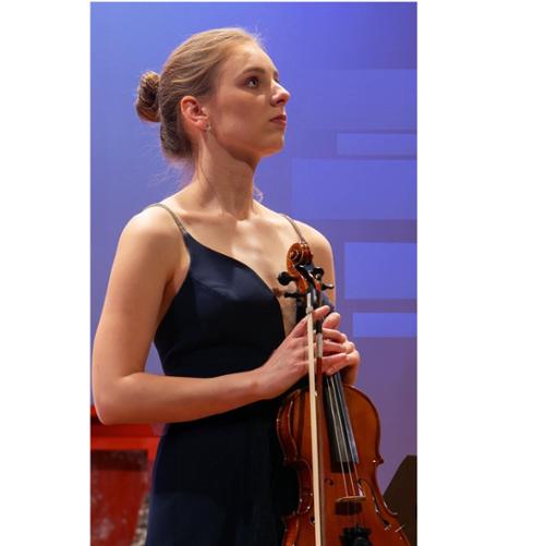 Zdjęcie kolorowe. Dziewczyna w stroju wieczorowym. Trzyma skrzypce. Niebieskie tło.