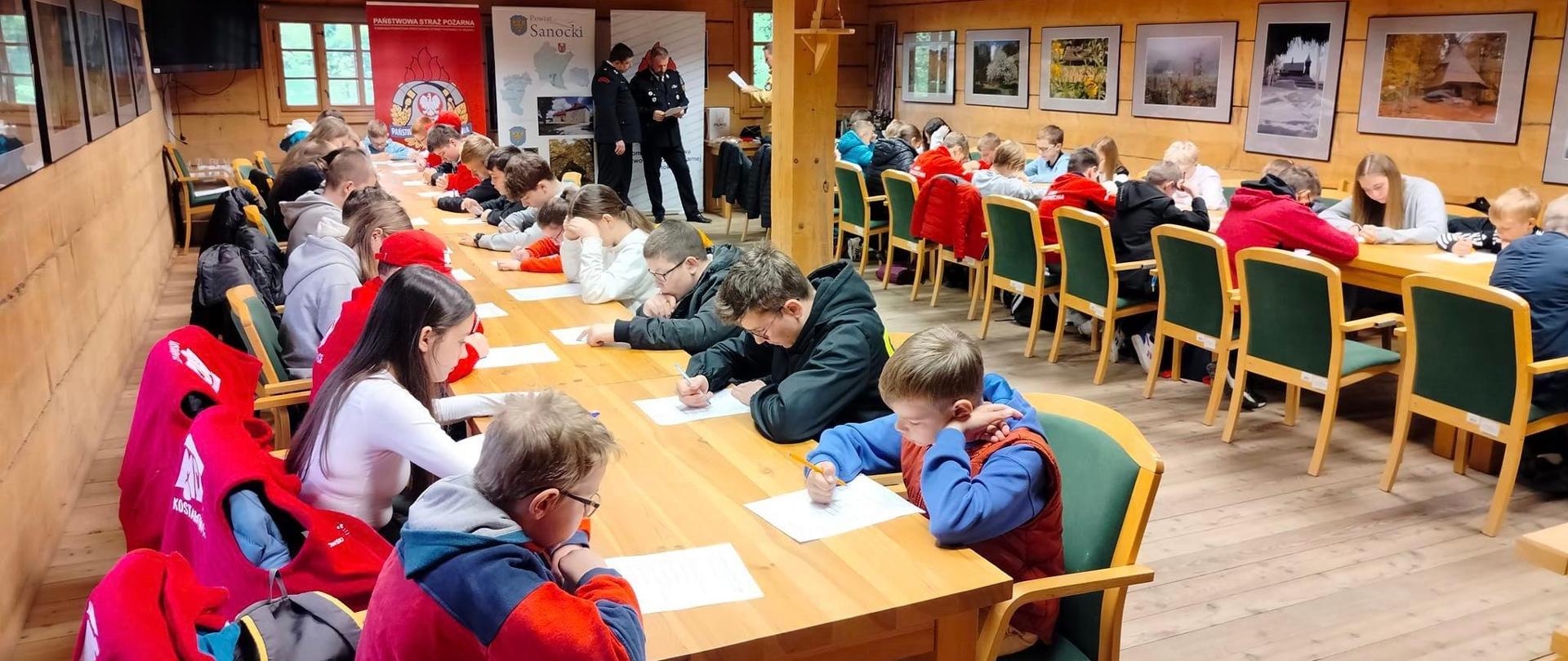 Zdjęcie wewnątrz pomieszczenia - przedstawia młodzież piszącą test.