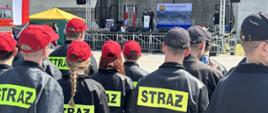 Zdjęcie przedstawia druhów OSP którzy stoją podczas obchodów dnia strażaka. Na scenie prezesi OSP witają zaproszonych gości 