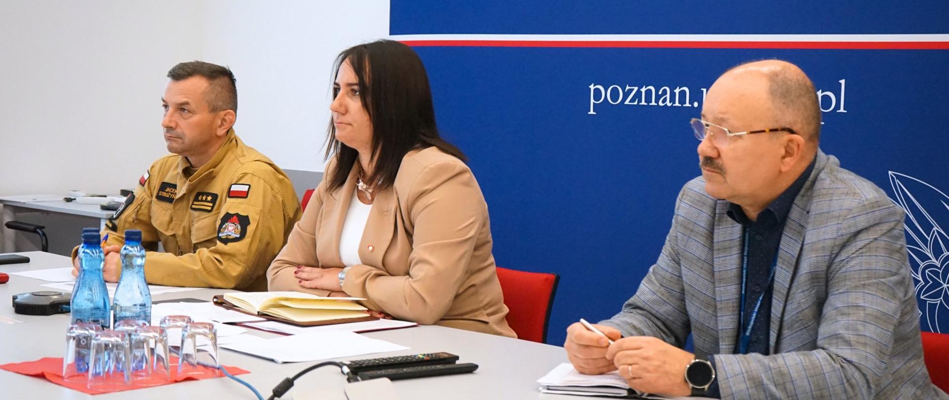 Pani Wojewoda, Pan Komendant oraz Pan Dyrektor zajęli miejsca za stołem i wsłuchują się w wideokonferencje, na sali w urzędzie.