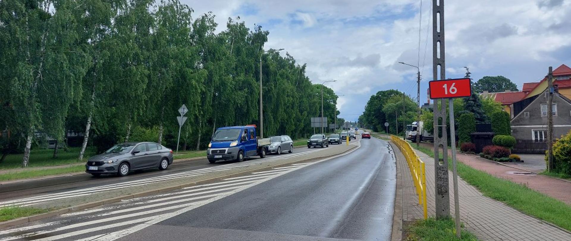 Droga krajowa nr 16 koło Augustowa, asfalt, pasy ruchu rozdzielone pasem rozdziału. Z boku czerwona tabliczka z numerem drogi. 