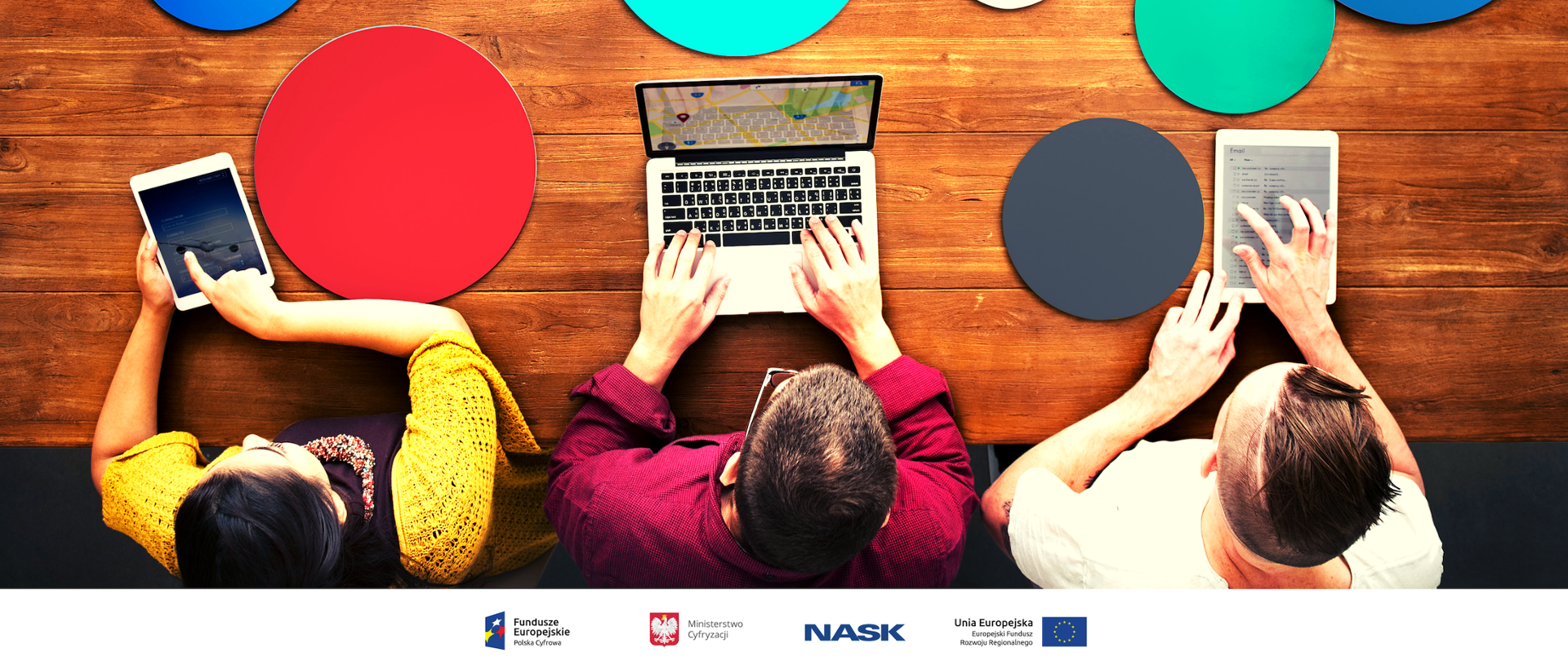 Trzy osoby w pozycji siedzącej. Jedna pracuje przy laptopie , a dwie pozostałe przy tablecie.