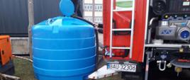 Widoczny zbiornik na wodę oraz uzupełniający go strażacy z pojazdu gaśniczego