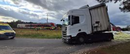 Na zdjęciu widać wypadek z udziałem pociągu i ciężarówki przewożącej cebule, która rozsypała się na drodze i poboczu. Na miejscu pracują służby ratunkowe, a w pobliżu stoją karetka i wozy strażackie. 