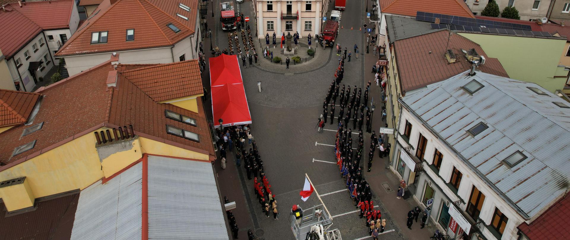 Zdjęcie przedstawia strażaków oraz zaproszonych gości stojących na placu podczas obchodów Dnia Strażaka