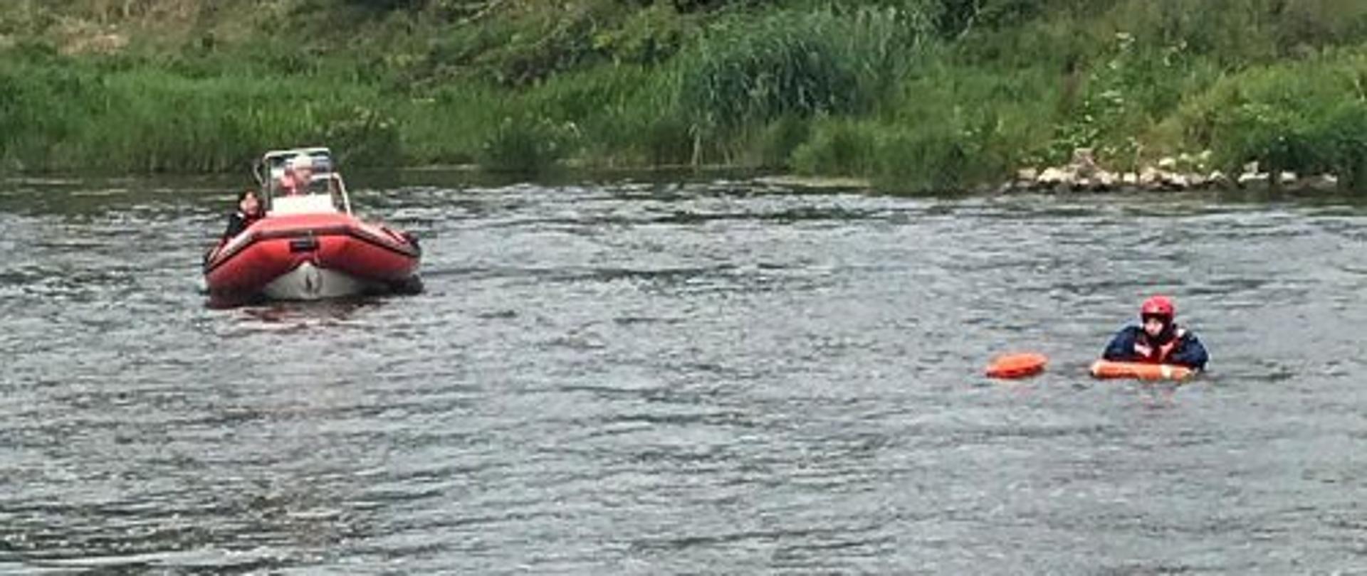 po rzece płynie łódź po lewej stronie dryfuje strażak w kapoku i z bojką