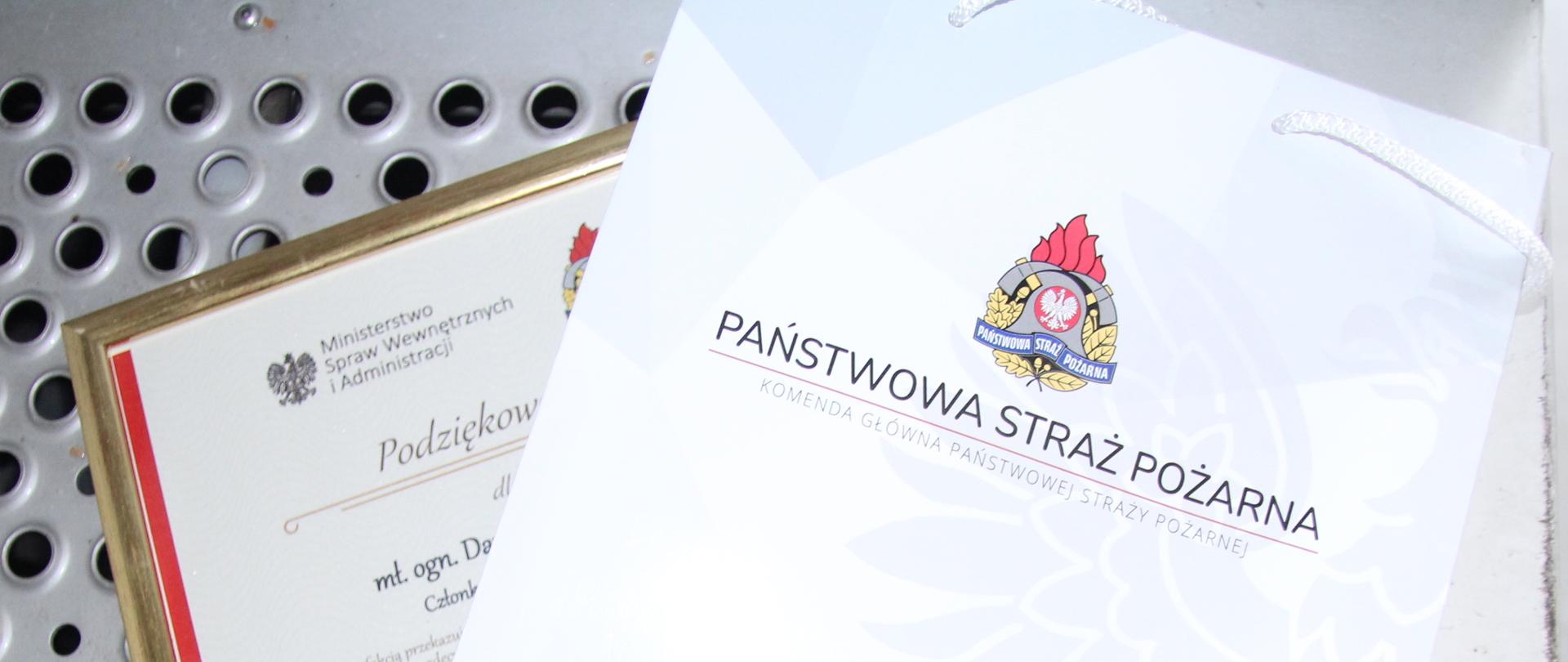 na schodach pojazdu pożarniczego leży podziękowanie oraz papierowa torba z napisem Państwowa Straż Pożarna 