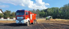 Na zdjęciu widać spalone pole, na którym było uprawiane zboże. Wypalenie jest w kolorze czarnym. W centralnym punkcie zdjęcia pojazd ratowniczo-gaśniczy w kolorze czerwonym z sygnalizacją ostrzegawczą, niebieską. Pojazd posiada oznakowanie białe. Niebo lekko zachmurzone, widać kolor błękitny. Zdjęcie wykonane w ciągu dnia.
