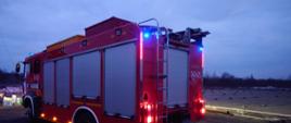 Zdjęcie wykonane wieczorem. Widać samochód ratowniczo-gaśniczy w kolorze czerwonym.