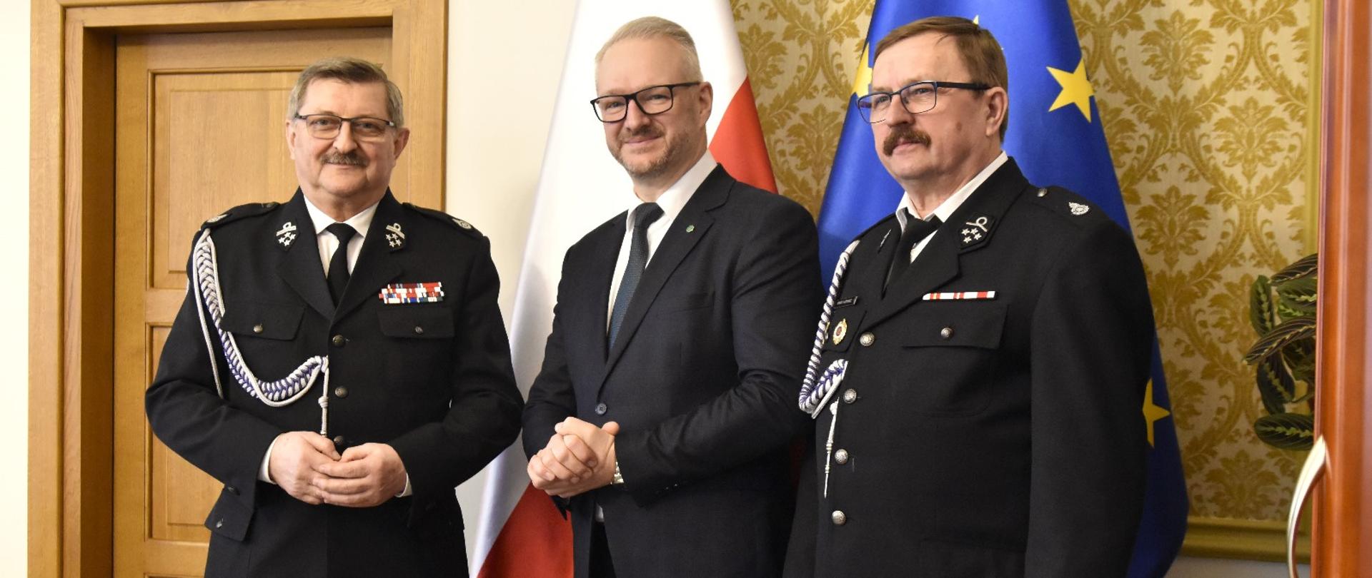 Trzech mężczyzn stoi na tle flag 