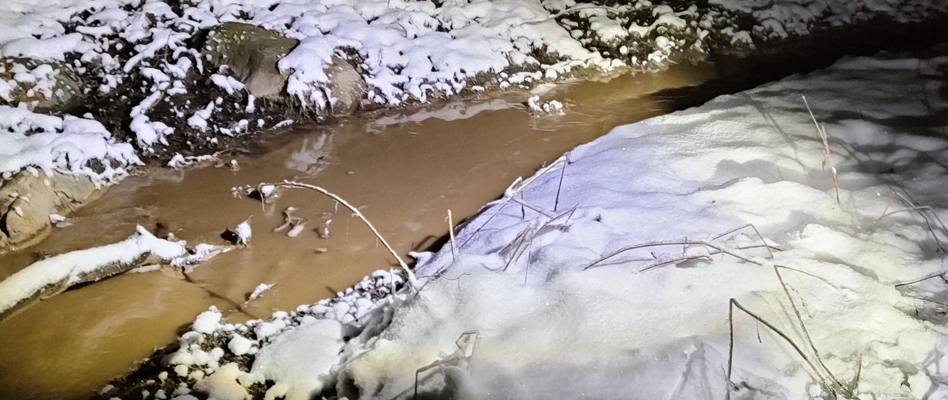 W nocy oświetlona część cieku wodnego z widocznym zanieczyszczeniem w postaci brązowego zmętnienia