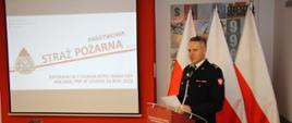 Strażak przemawia przy mównicy obok wyświetalan jest prezentacja multimedialna.