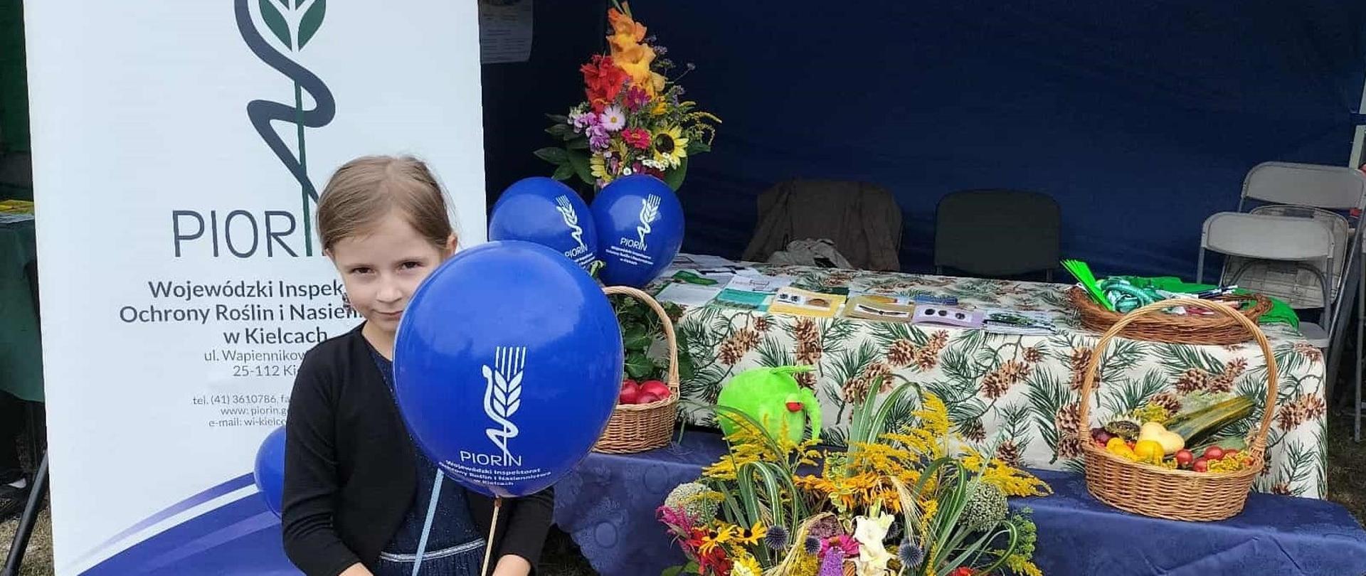 Na tle stoiska promocyjnego stoi dziewczynka z balonem z logo PIORiN.