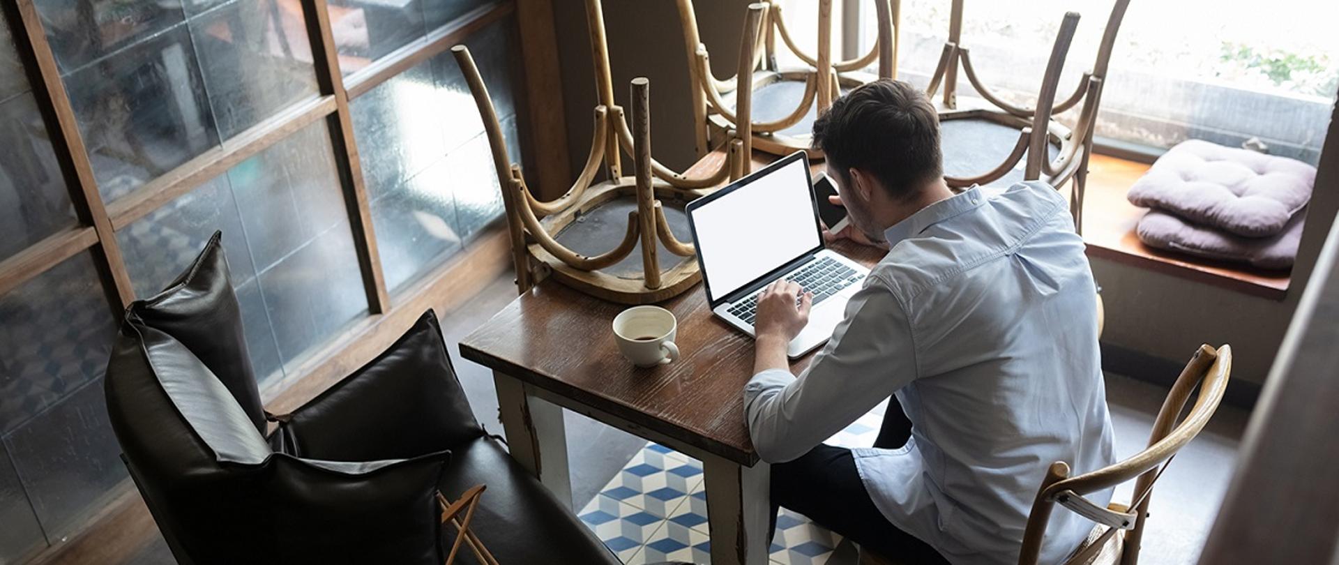 Mężczyzna siedzący przed laptopem, na stole postawione do góry dnem krzesła 