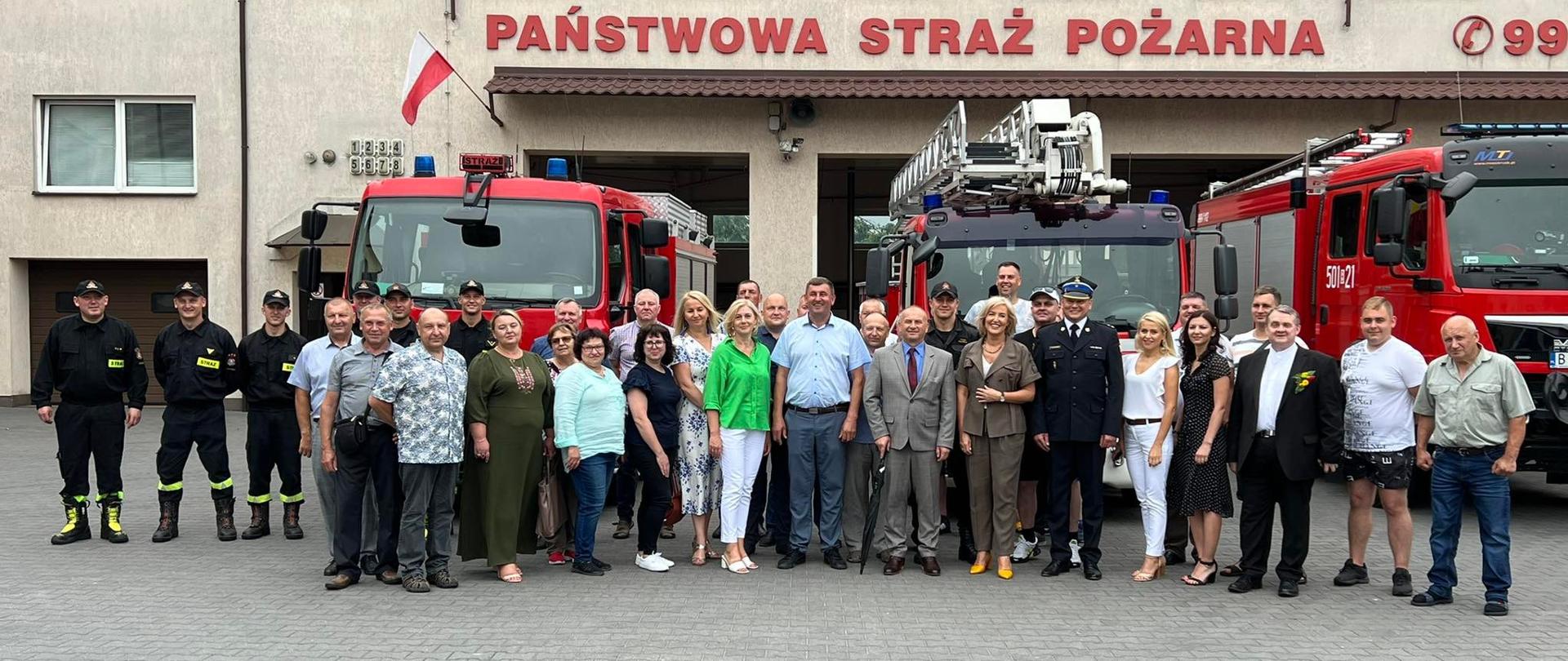Przedstawiciele litewskiego powiatu szyrwinckiego podczas wizyty w KP PSP w Zambrowie ustawieni do zdjęcia w tle samochodów ratowniczo-gaśniczych