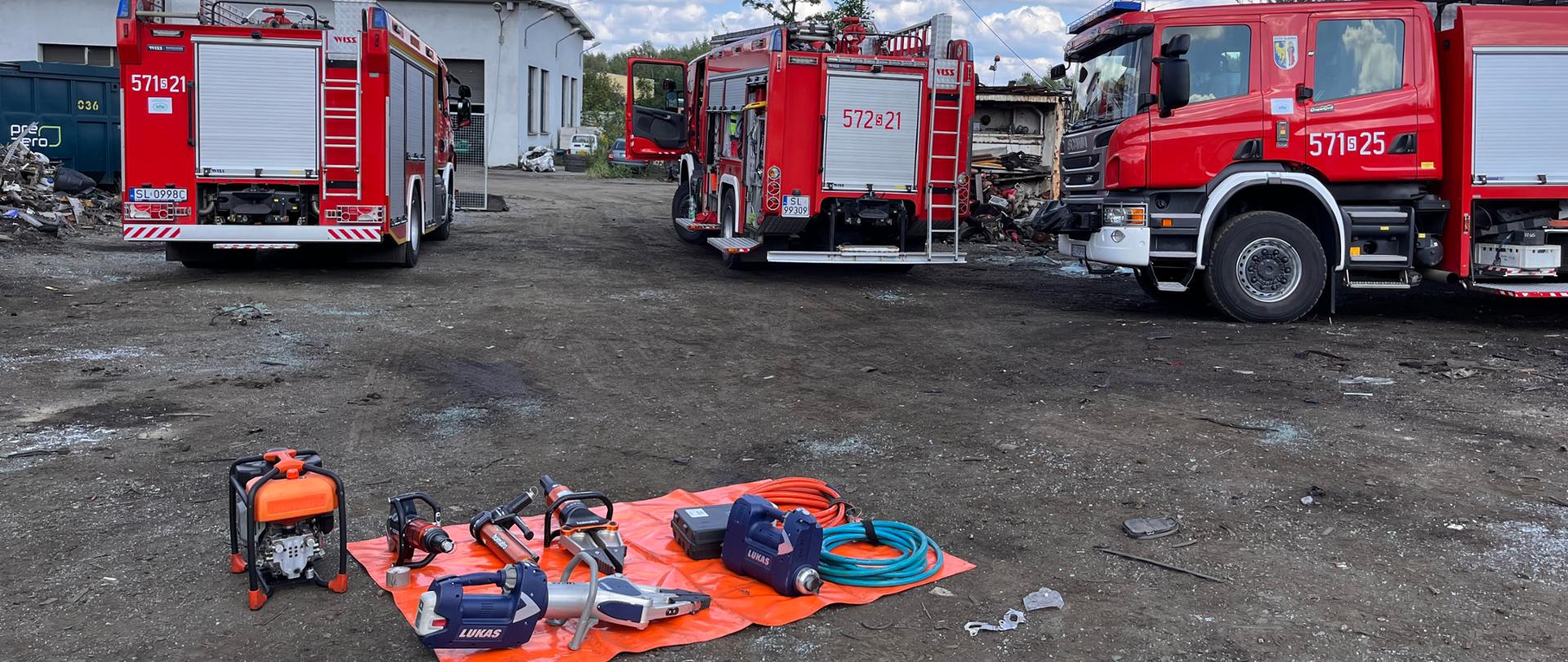 Zdjęcie przedstawia samochody pożarnicze oraz przygotowane pole sprzętowe do ćwiczeń.