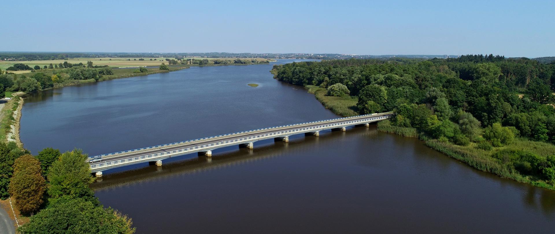 Na zdjęciu widać most drogowy dziewięcioprzęsłowy na rzece. Brzegi rzeki porośnięte lasami.