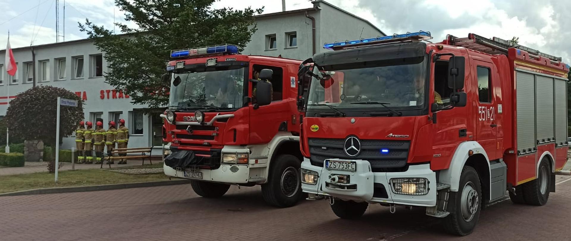 Zdjęcie przedstawia dwa samochody ratowniczo-gaśnicze z włączonymi światłami mijania oraz sygnałami świetlnymi. auta znajduja się przed budynkiem komendy PSP w Świdwinie.