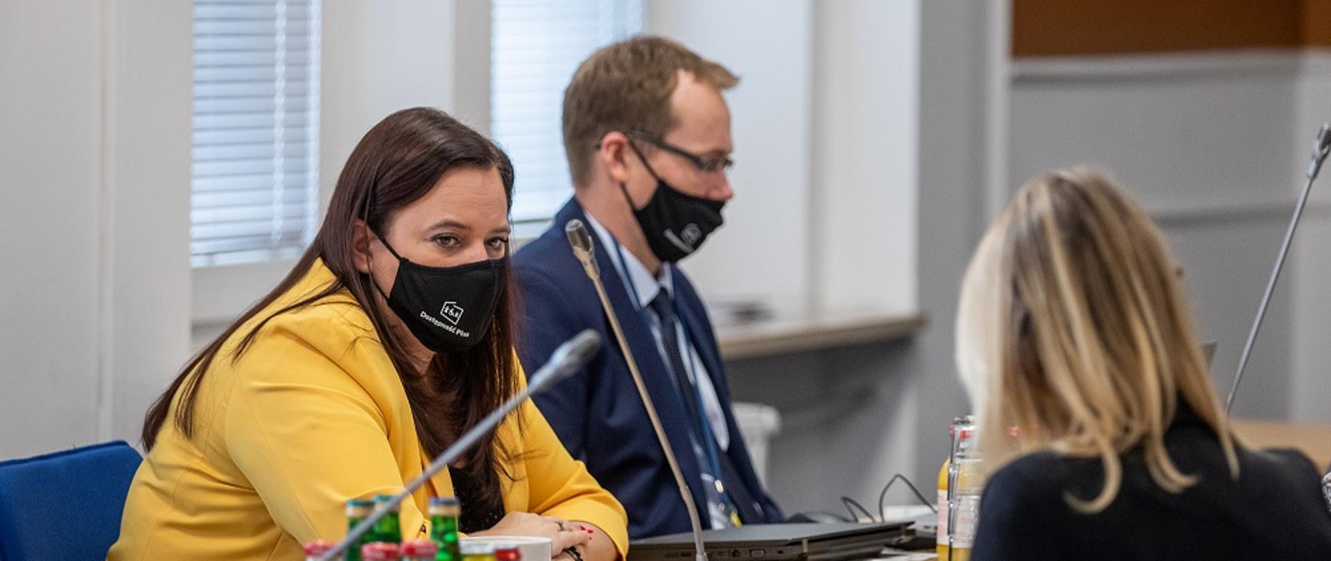 Na zdjęciu widoczne trzy osoby - mężczyzna i kobieta siedzą przy stole konferencyjnym, naprzeciwko nich, tyłem, siedzi druga kobieta. 