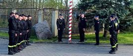 Strażacy stoją na baczność oddając honory podczas wciągania flagi Polski na maszt.