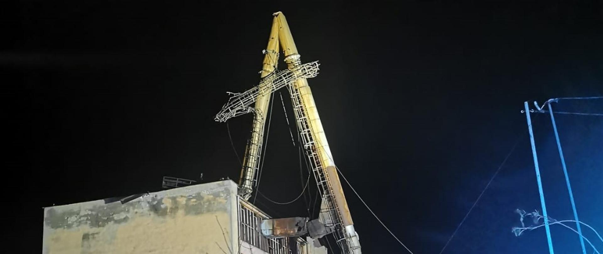 Na zdjęciu złamana metalowa konstrukcja komina nieczynnej ciepłowni miejskiej. Złamana część wspiera się na betonowym stropodachu budynku ciepłowni. 
