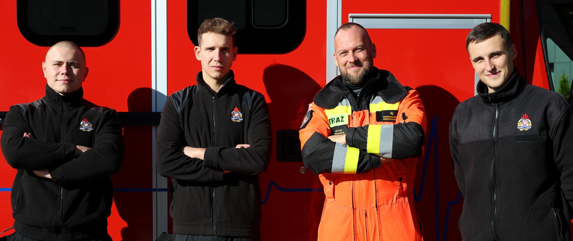 1. Mistrzostwa Pierwszej Pomocy - czterej strażacy biorący udział w wydarzeniu na tle samochodu