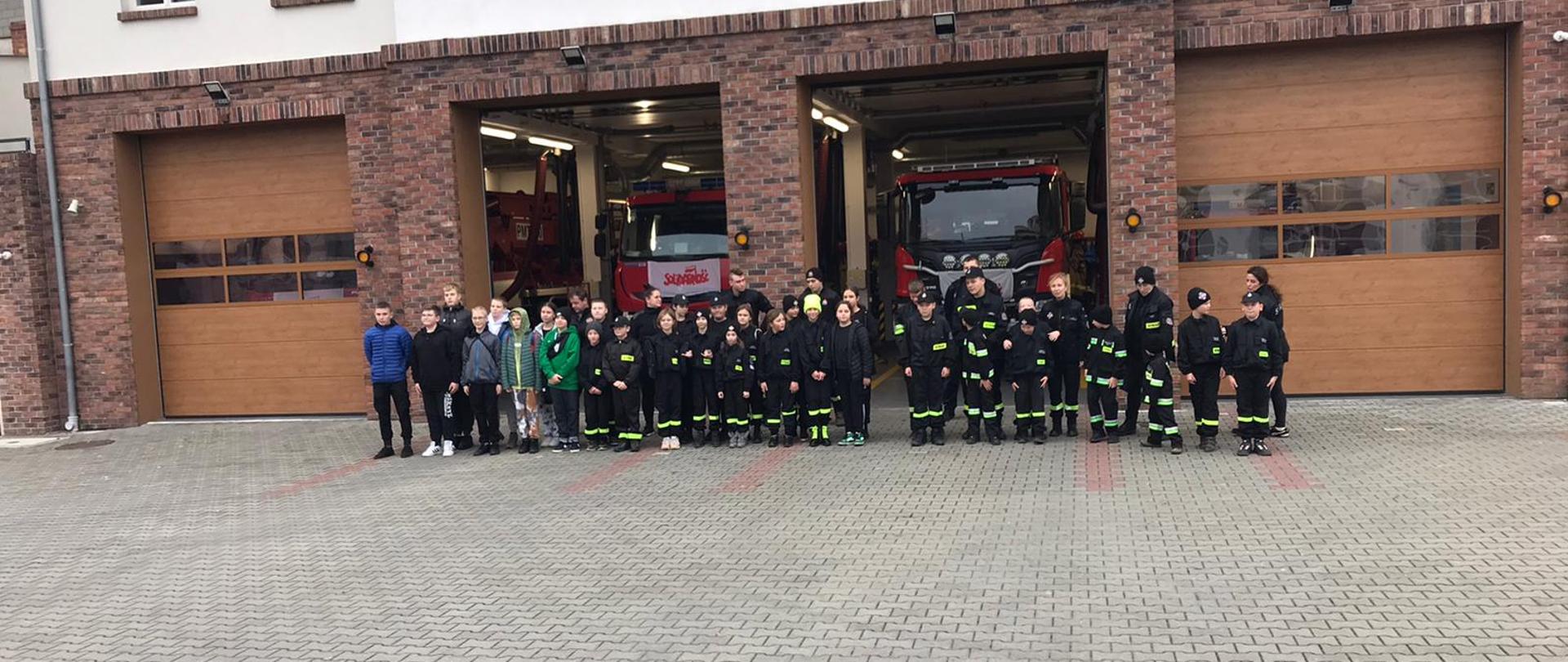 Na zdjęciu widać grupę dzieci z młodzieżowych drużyn pożarniczych na tle strażnicy w Pucku.