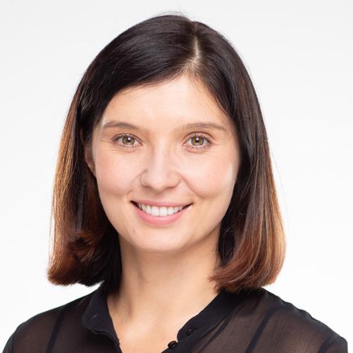 Młoda około czterdziestoletnia kobieta uśmiechnięta, ma ciemne oczy oraz krótkie do ramion włosy w kolorze brąz. Ubrana w czarną elegancką koszulę. 