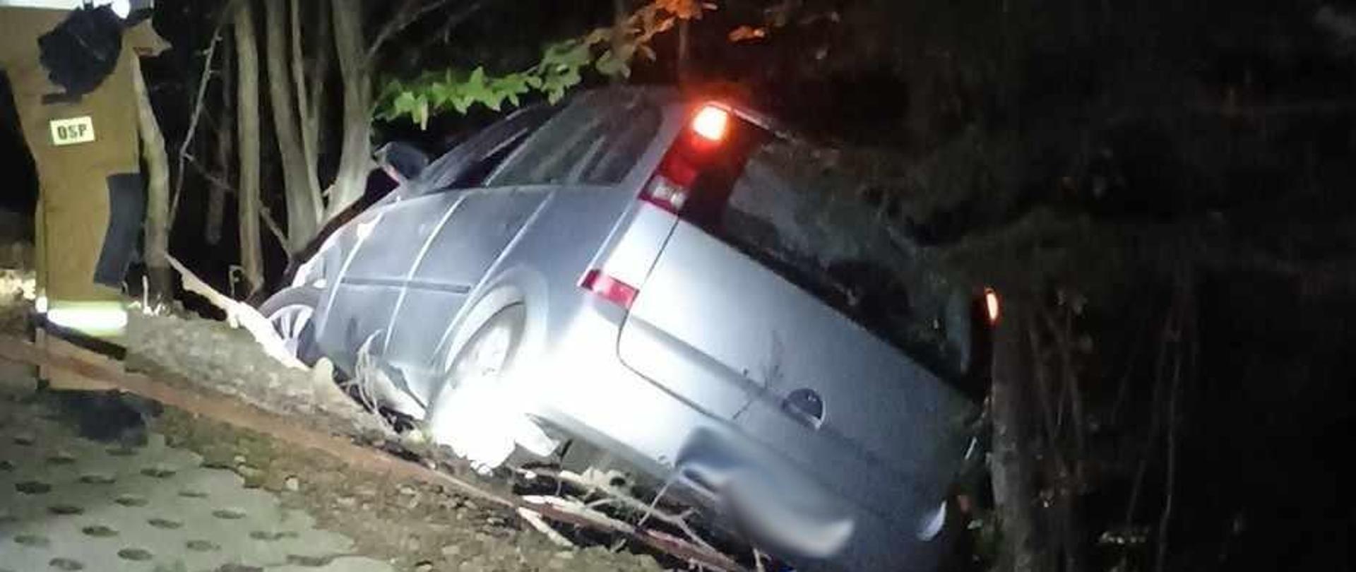 Samochód osobowy poza drogą a obok strażak