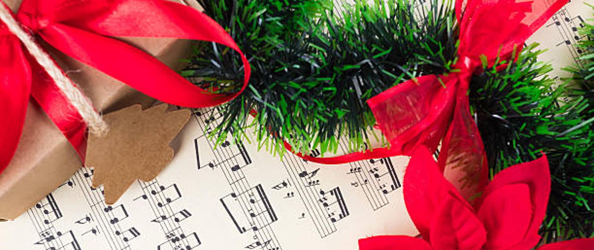 Christmas ornament and music sheet on white natural wooden table. Red ribbon bow. Poinsettia. Gift or present with label and twine.