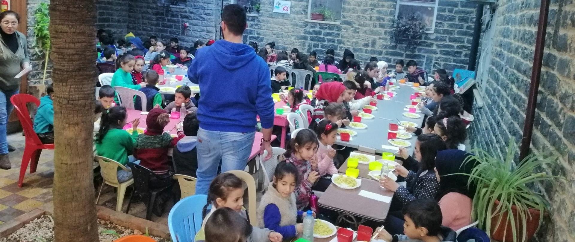 dzieci siedzą przy stole i jedzą posiłek