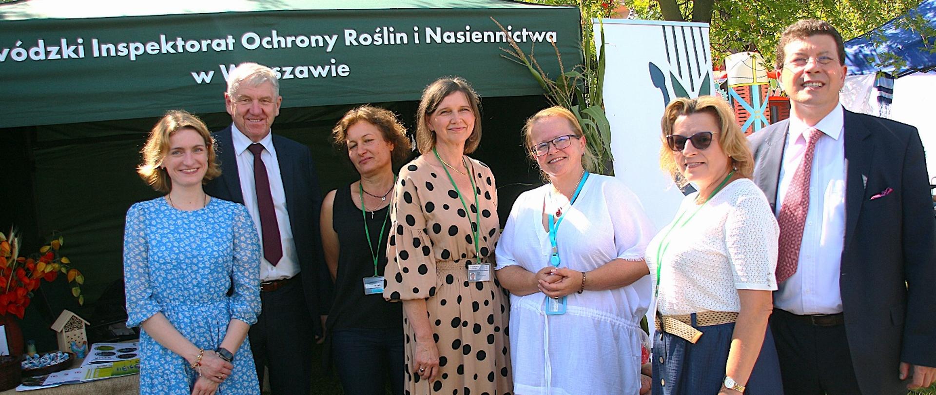 Grupa pracowników i gości przed stoiskiem Wojewódzkiego Inspektoratu Ochrony Roślin i Nasiennictwa w Warszawie.