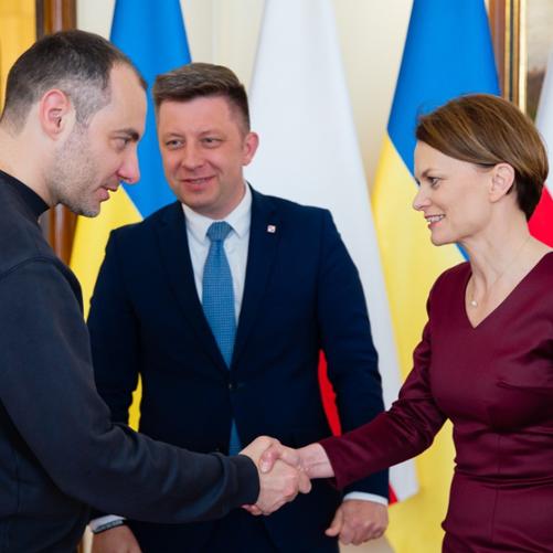 Trzy osoby rozmawiają ze sobą i ściskają sobie dłonie.