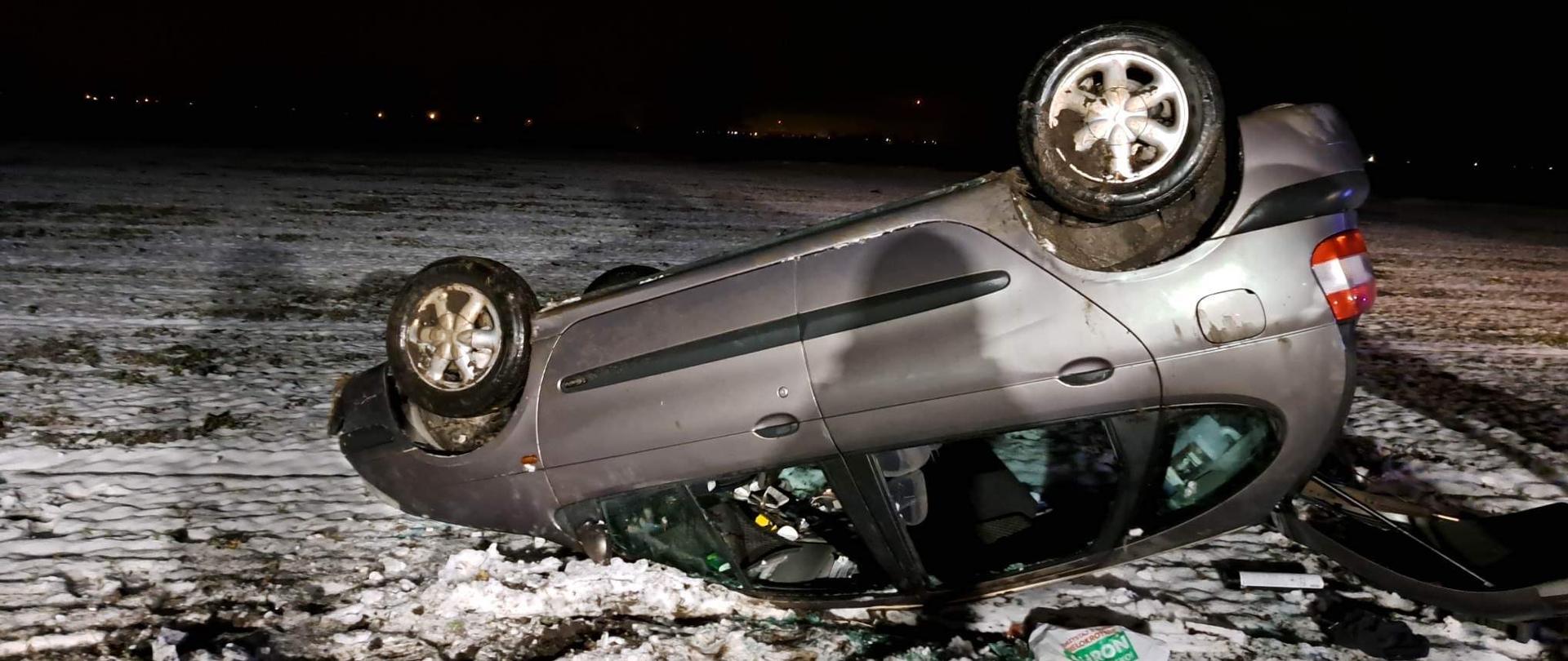 Samochód osobowy po dachowaniu leży na zaśnieżonym polu