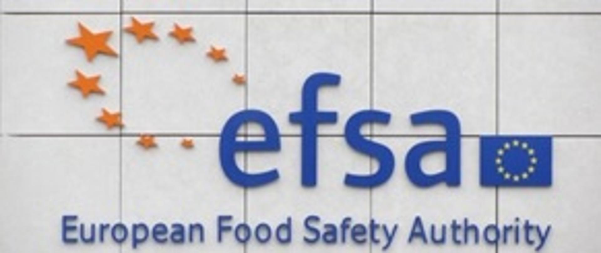 Logo organizacji EFSA European Food Safety Authority. Na szrym tle w fomie kafelek napis sfsa - po prawej na wyskości litery a - flaga uE.
Pod nią napis: European Food Safety Authority