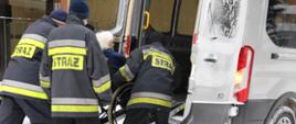 Na zdjęciu widać jak strażacy pomagają starszej osobie dotrzeć na szczepienie 