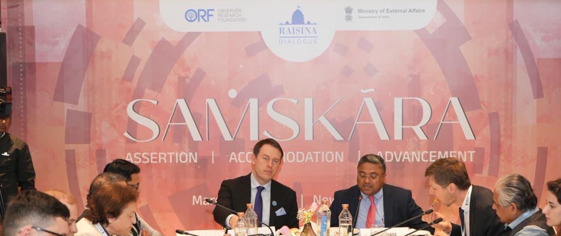 Uczestnicy siedzą przy stole podczas dyskusji panelowej zorganizowanej wspólnie przez PISM i ORF podczas Raisina Forum 2026. Na czele stołu stali Podsekretarz Stanu w Ministerstwie Rozwoju i Technologii Rzeczypospolitej Polskiej Pan Michał Baranowski i Wiceministrem w Ministerstwie Spraw Zagranicznych Republiki Indii Sibi George.