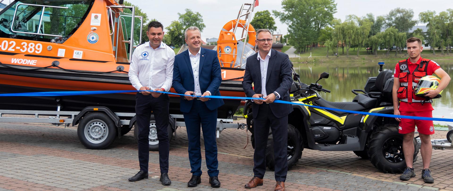 
Grupa osób stojąca na tle sprzętu do ratownictwa wodnego
