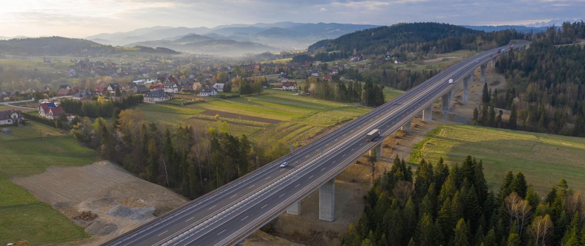 Dwupasowa estakada. W tle widoczne zabudowania, a w oddali góry. Pogoda wiosenna, dzień.