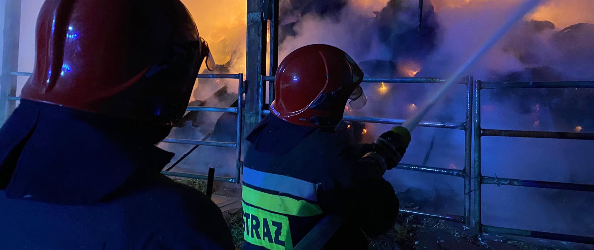 Pożar słomy magazynowanej w budynku gospodarczym o wymiarach 30 x 15 x 7 m w Kopaniewie w gminie Wicko. Dwaj strażacy podają prąd gaśniczy w natarciu do wnętrza palącego się budynku. We wnętrzu widoczne płomienie. Panuje silne zadymienie. Działania prowadzone w porze nocnej.