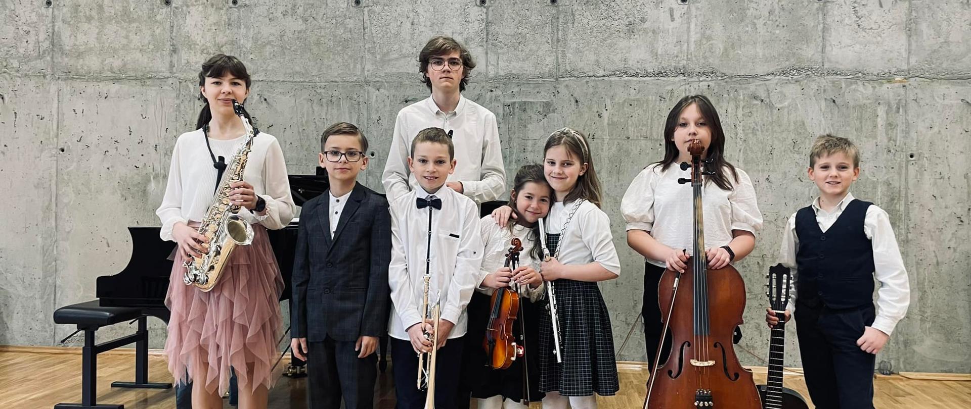 Grupa uczniów z instrumentami w rękach na tle sali koncertowej
